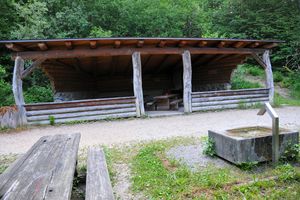 Aussenansicht der Waldhütte Spilwald mit Brunnen, Tisch und Bänken im Freien